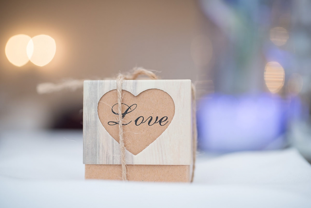 Wedding FAQS - wedding favour box with text that says 'love' enclosed within a heart shape and tied with string, on a table