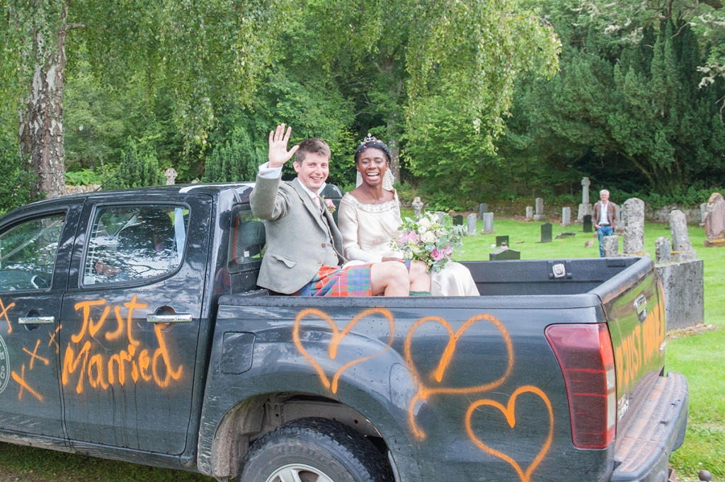 Wedding FAQS - bride and groom sitting outside on the back of a black truck with orange spray paint that says 'just married'