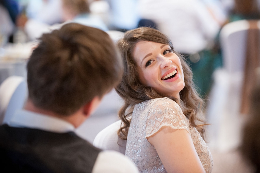 Wedding FAQS - bride with her head tilted backwards as she makes eye contact with her groom and laughs, sitting at a table
