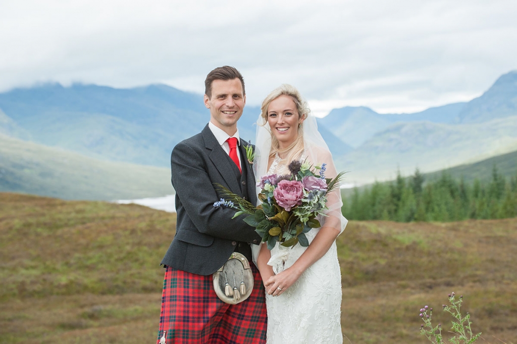 Wedding photography prices - bride and groom holding a bouquet of flowers with a lake, trees and mountains in the background