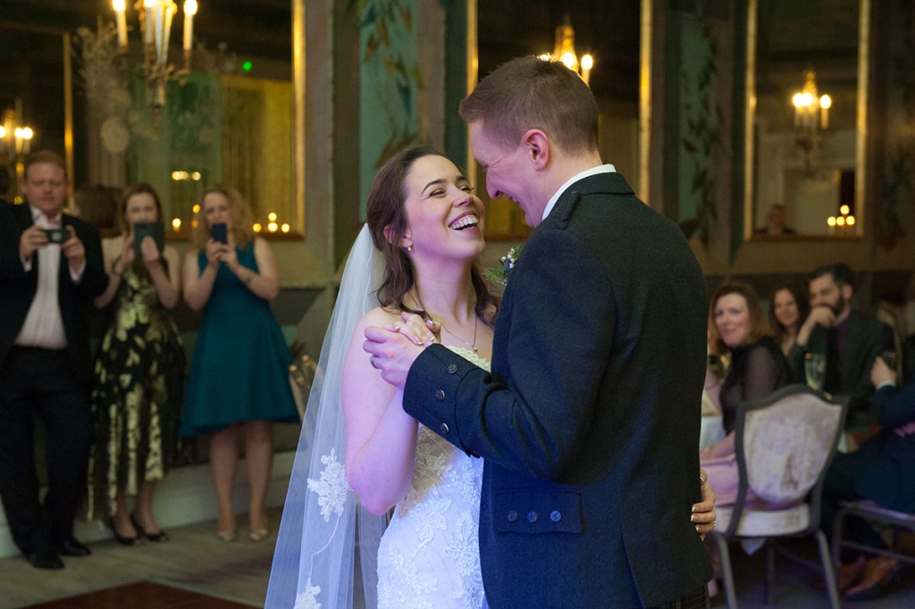 Documentary wedding photograph of a bride laughing as she dances with her groom, as wedding guests look on with mobile phones