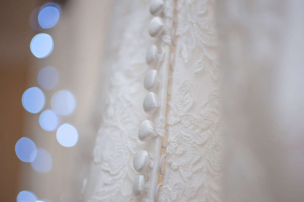 Buttons on the back of a white wedding dress with blue bokeh fairy lights, taken by a documentary wedding photographer