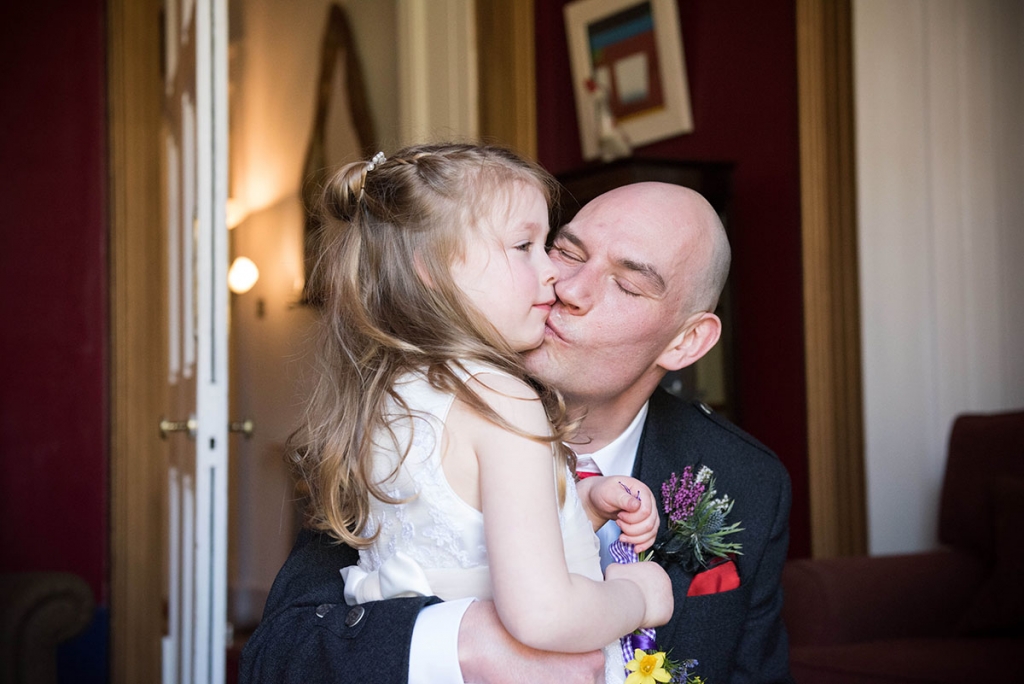 Groom crouching down to kiss his young daughter, captured by a documentary wedding photographer