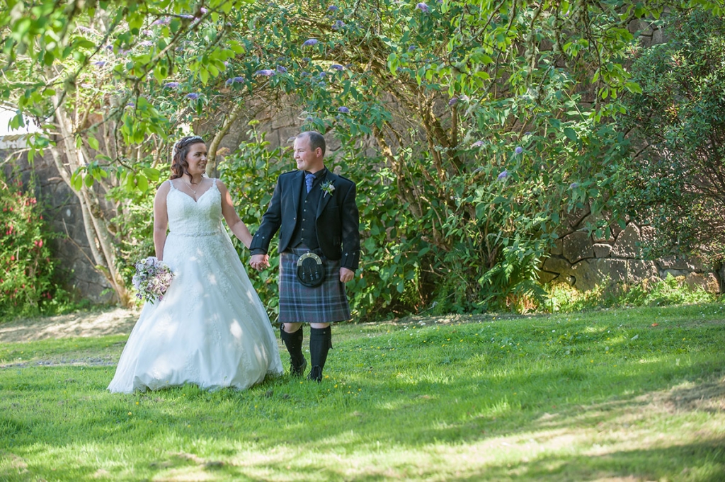Wedding photo of a bride and groom holding hands and walking on a lawn beneath a beautiful floral display
