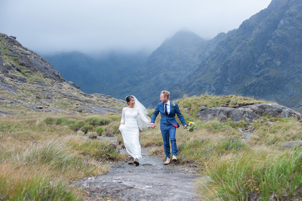 Bride and groom holding hands and looking at each other while walking in a mountainous landscape