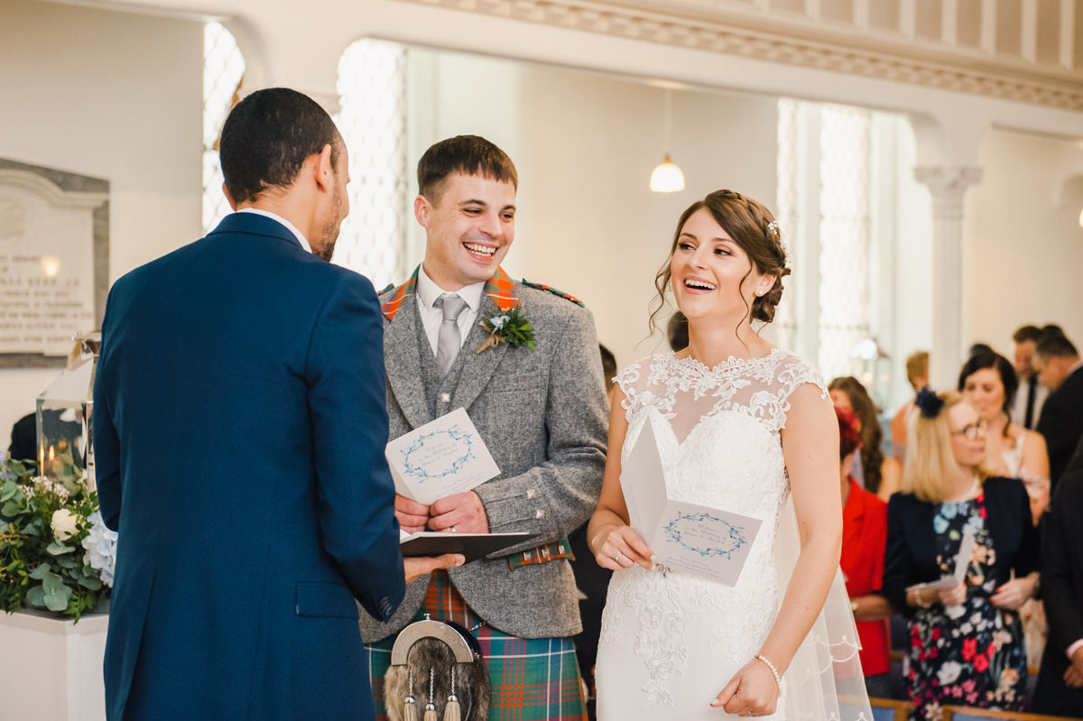 A bride and groom laughing during their wedding ceremony in a church, in front of wedding guests