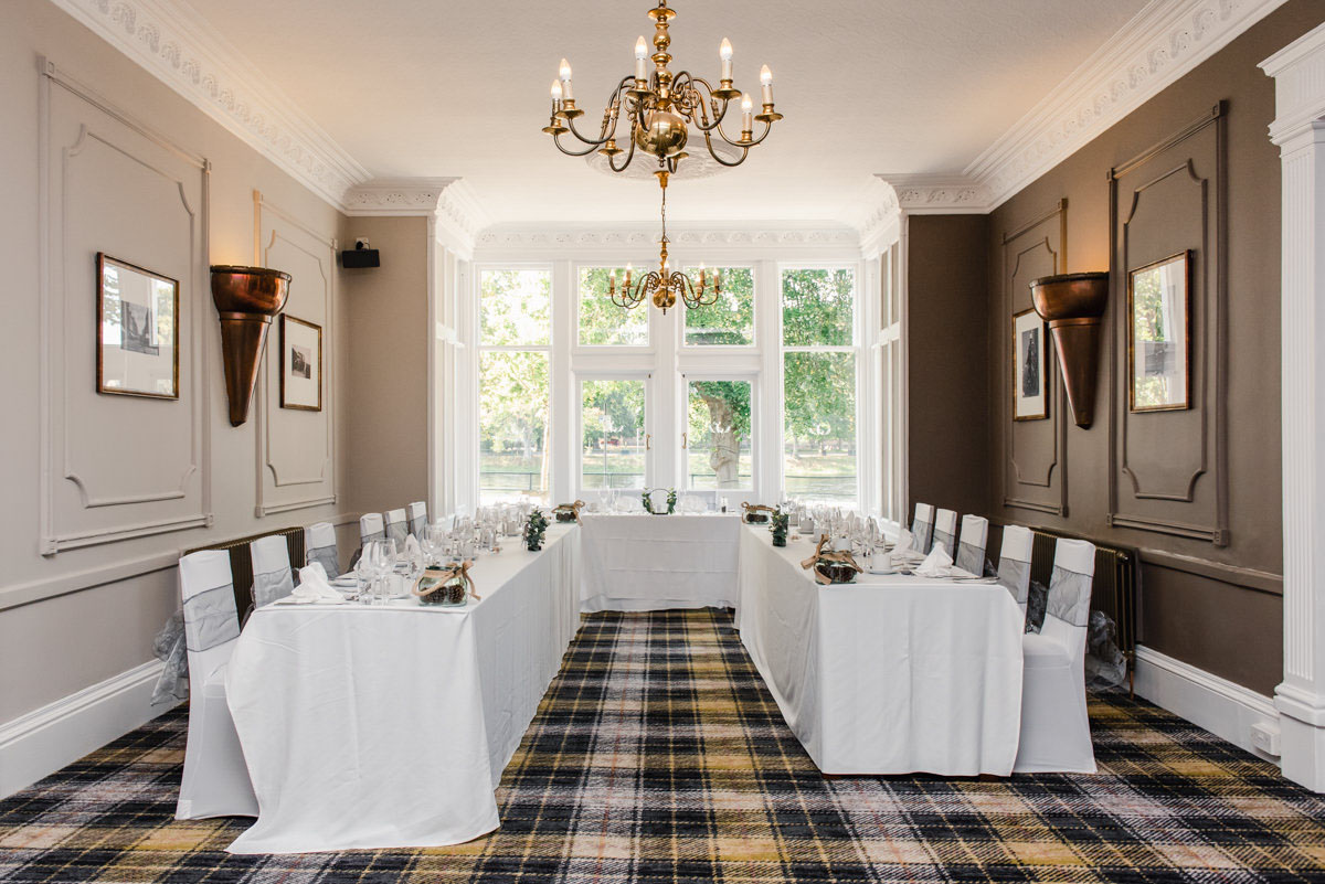 A rectangular hotel suite with a tartan carpet and beige walls, decorated for a wedding with a table and chairs