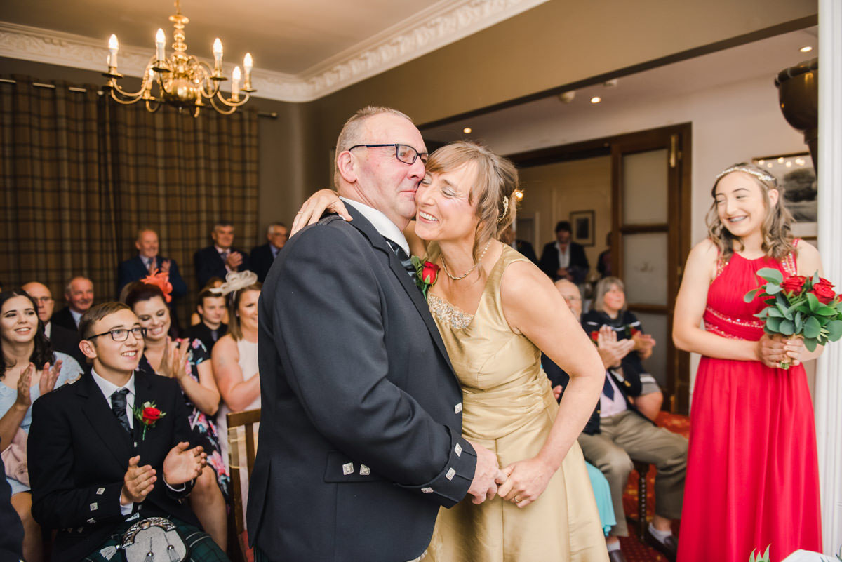 An emotional bride and groom kissing during their wedding ceremony in front of their guests in a small function room