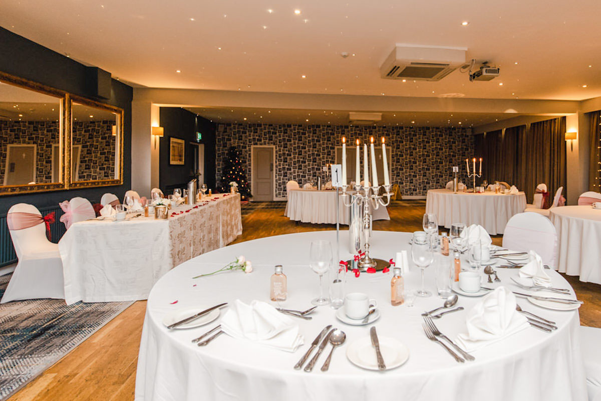 A function suite decorated for a wedding with round white tables with candle centrepieces and a rectangular top table