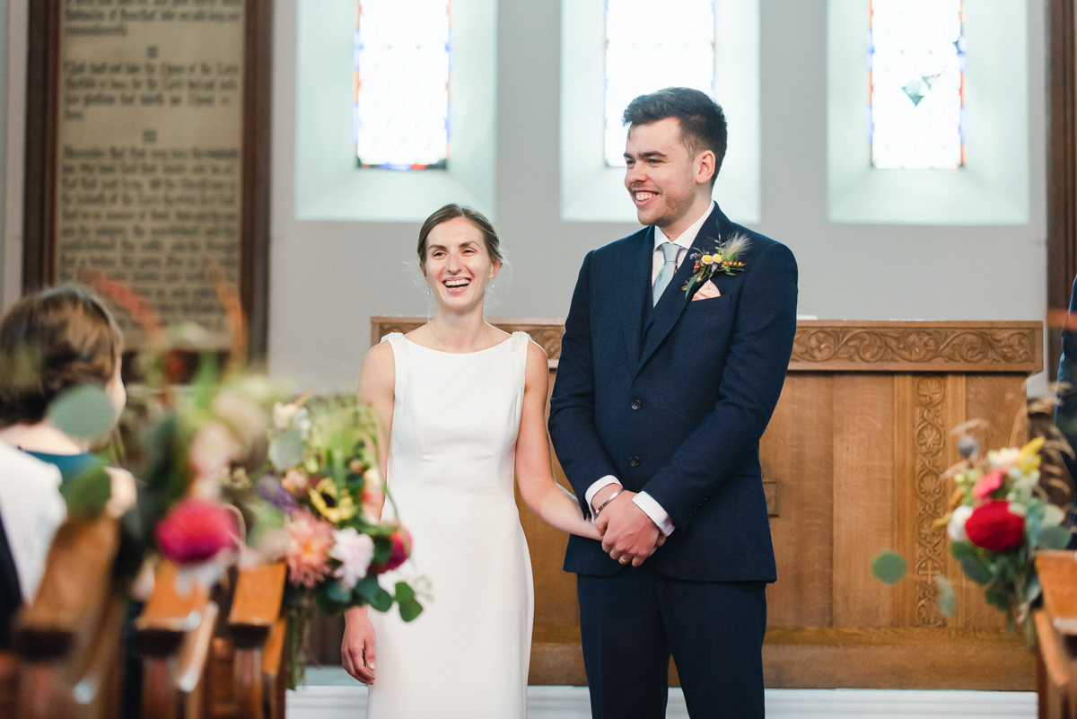 Candid wedding photograph of a bride and groom smiling and holding hands in their church wedding ceremony in the Highlands
